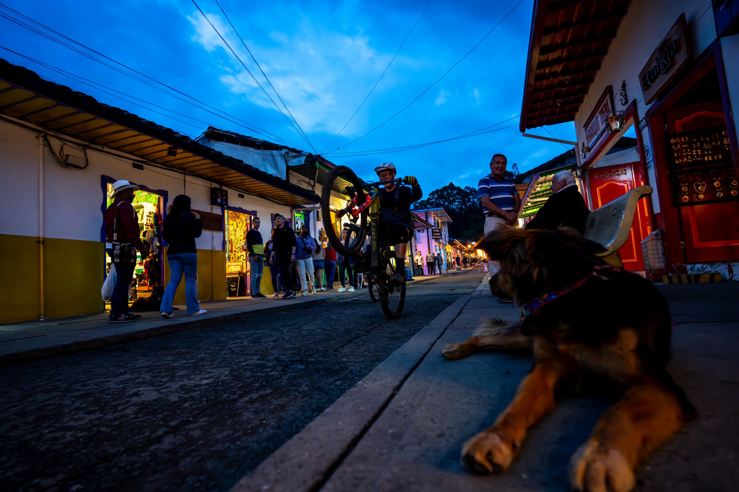 Cyclist performs a wheelie in a vibrant Colombian street, showcasing local culture. Taste of Colombia, Scotty Laughland ambiance. Mountain Bike United.