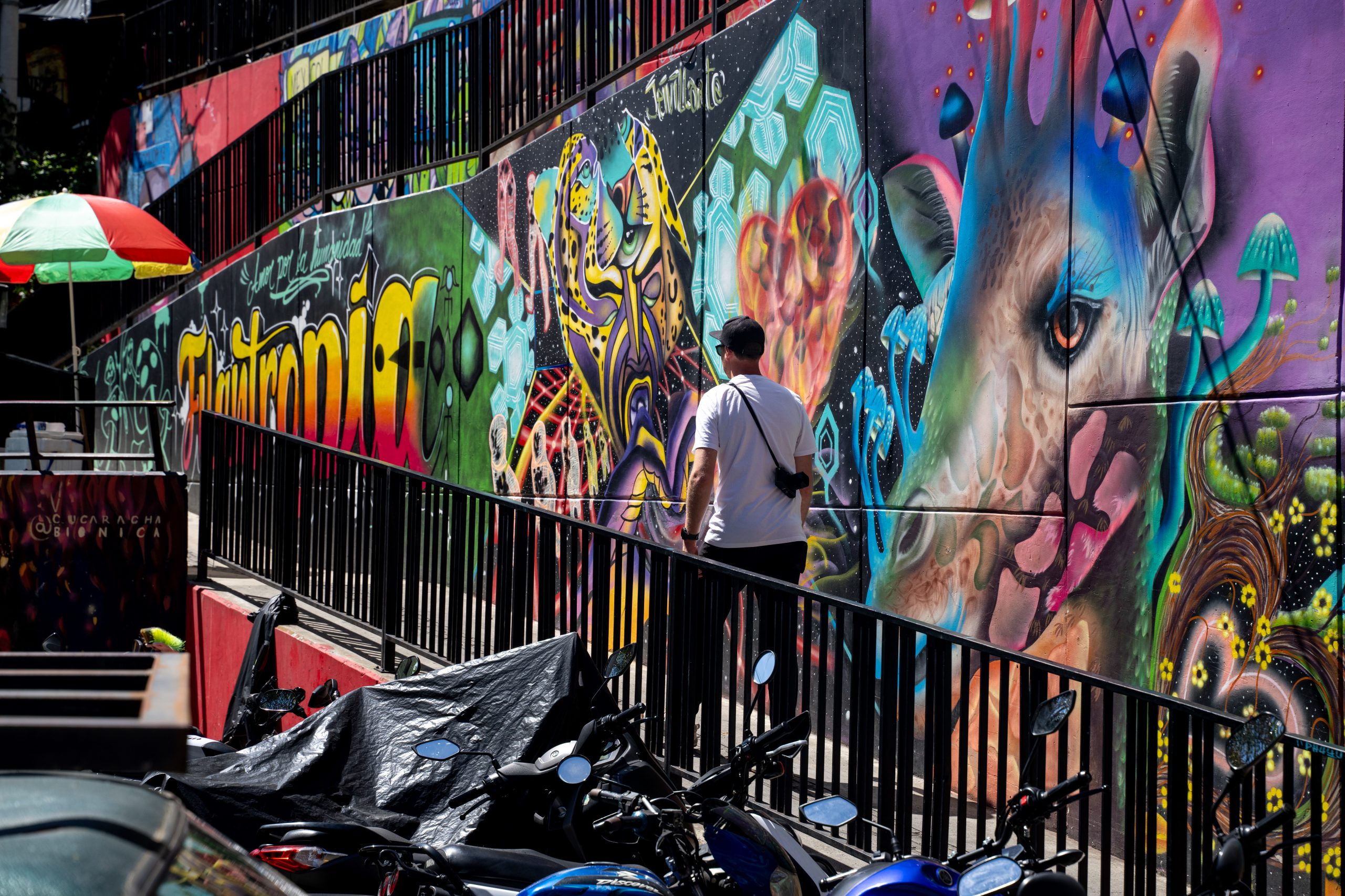Street art in Colombia showcasing vibrant graffiti with a person walking by. Keywords: Taste of Colombia, Scotty Laughland, colorful murals. Mountain Bike United.