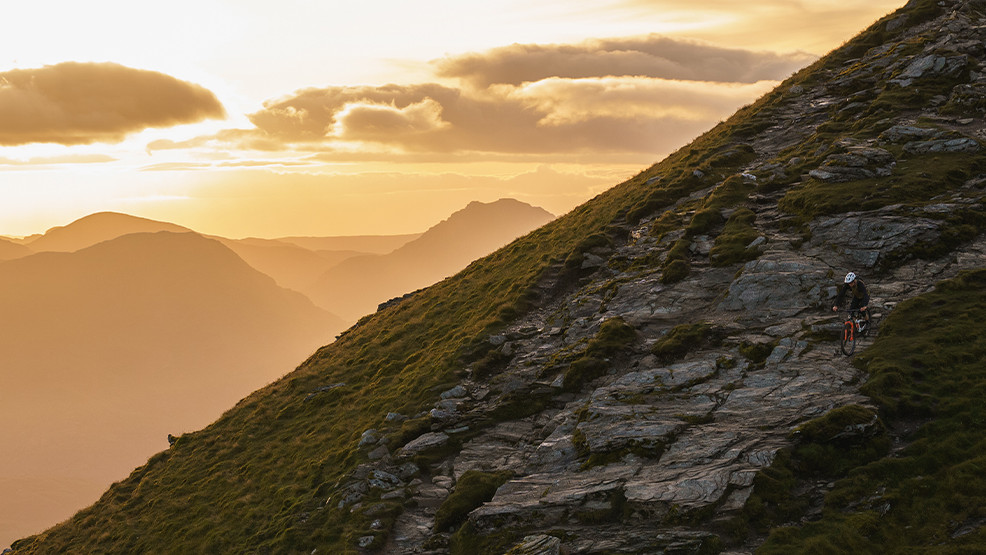 Mountain biking at sunset on a rugged Scottish hillside, featured in Scotty's Scotland Showcase Season 2. Scenic adventure landscape. Mountain Bike United.