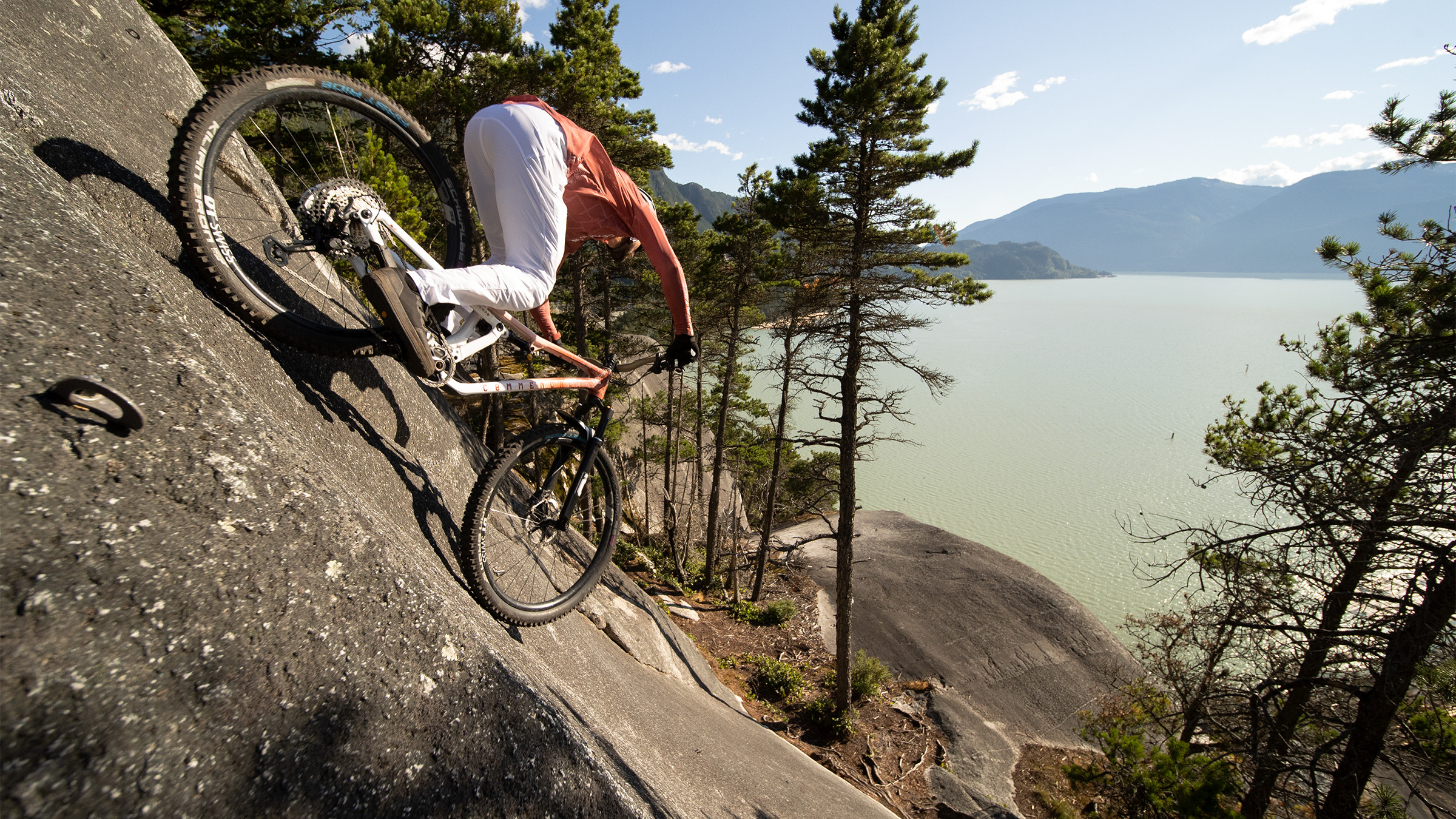 Mountain biker navigates steep terrain near a lake, showcasing cross country adventure and skill. Explore outdoor thrills with Kilian Bron. Mountain Bike United.