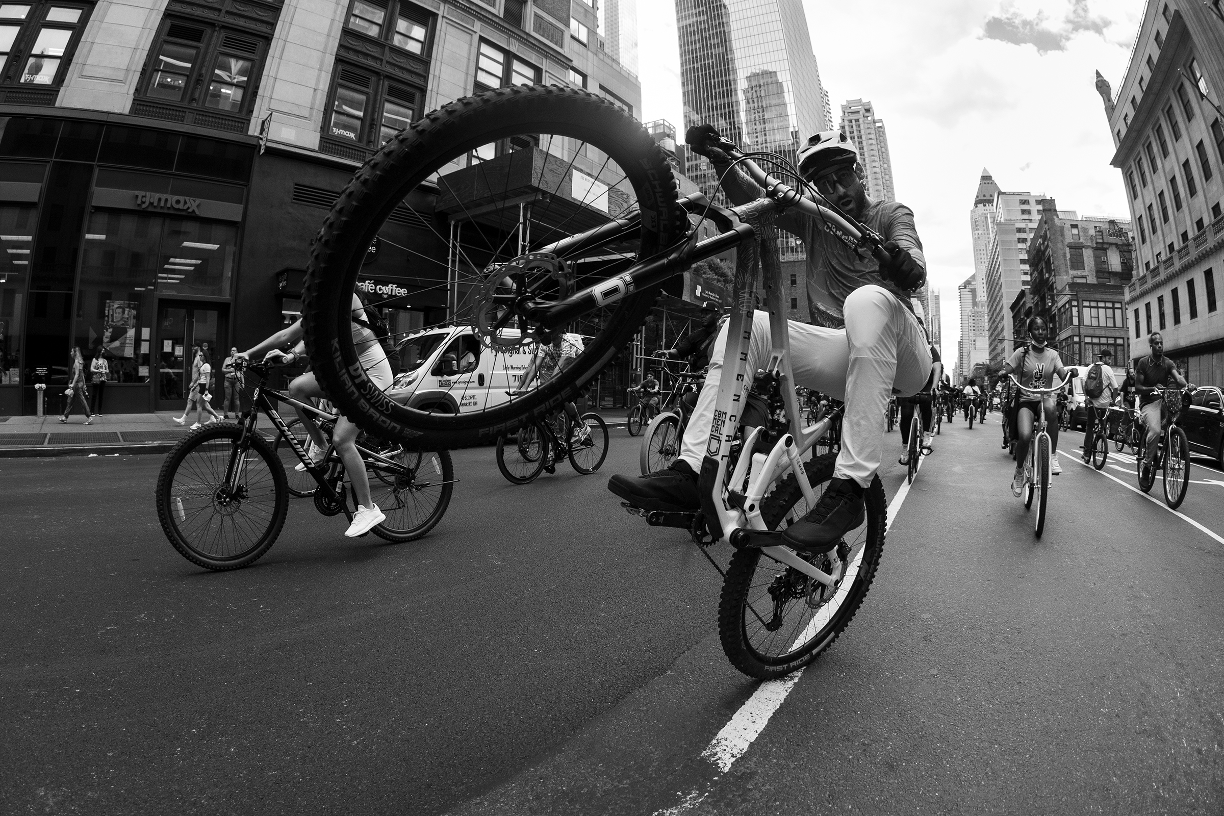 Cyclist performs a wheelie in an urban group ride, highlighting cross countries biking excitement inspired by Kilian Bron's adventures. Mountain Bike United.