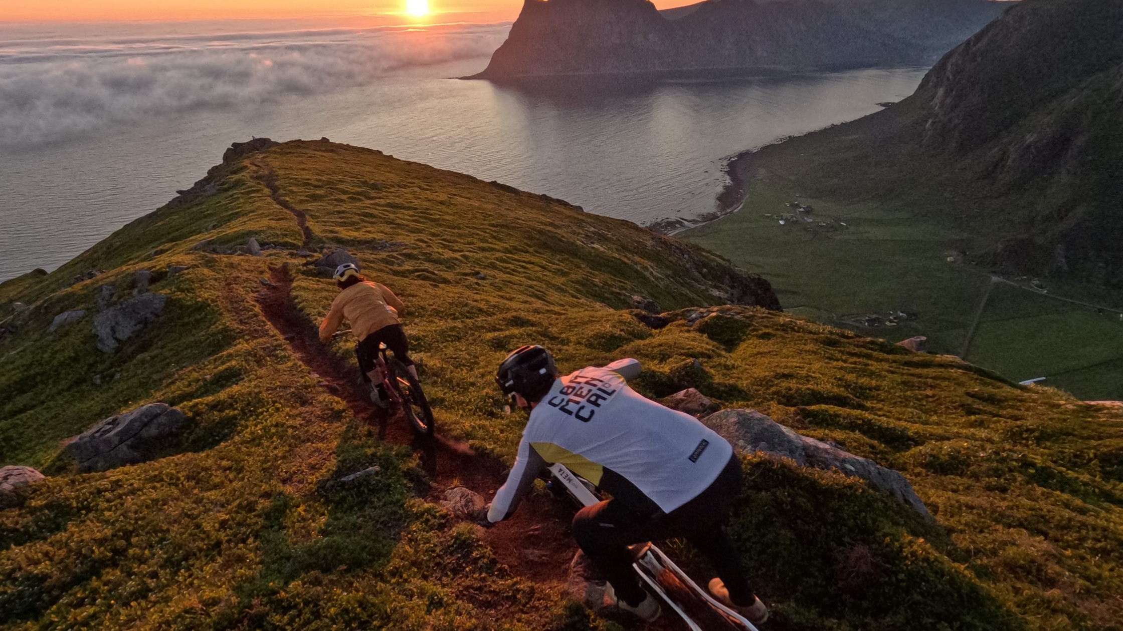 Mountain bikers ride along a scenic ridge trail at sunset, overlooking the ocean and dramatic cliffs, embodying adventure and nature exploration. Mountain Bike United.