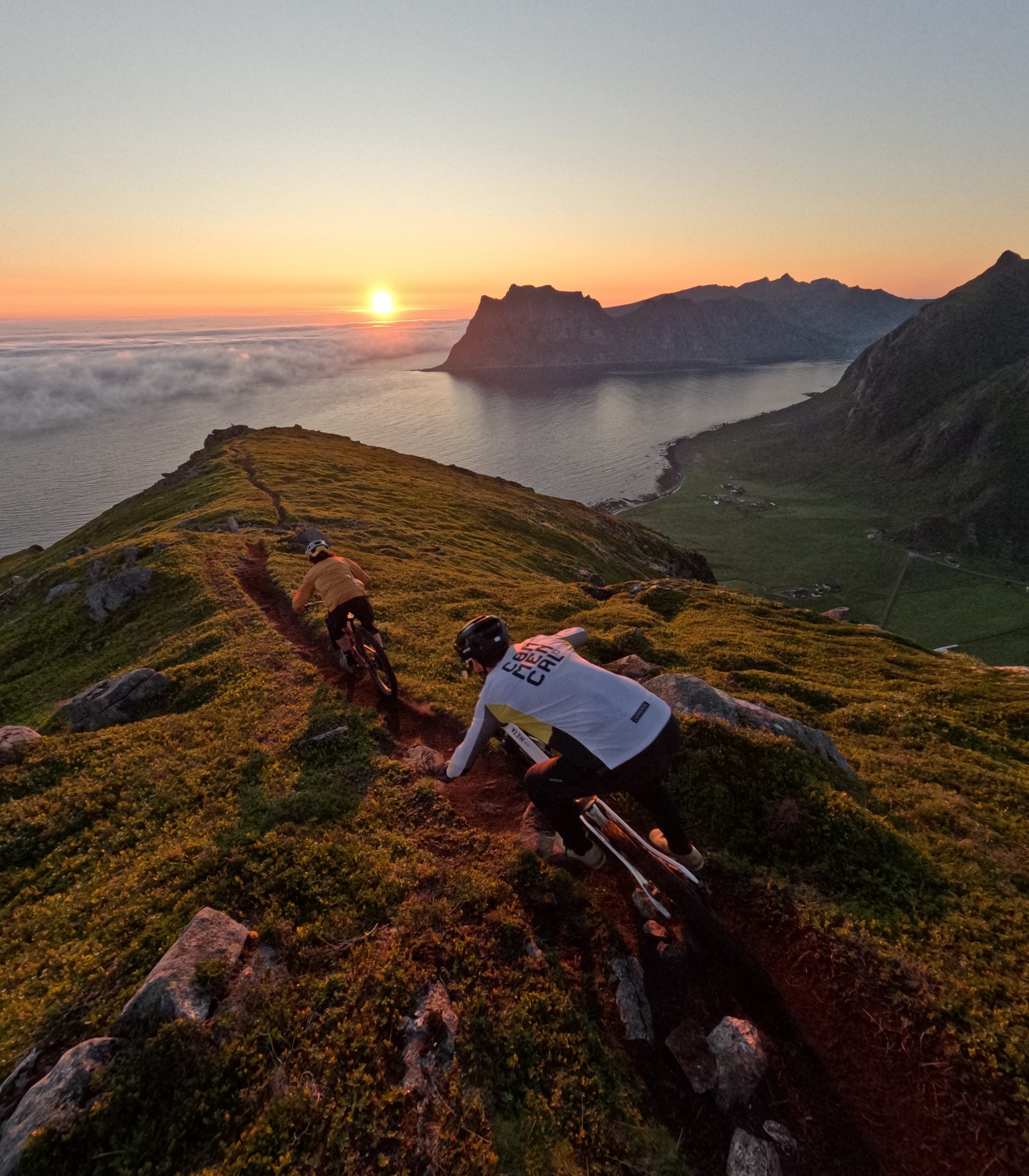 Mountain bikers ride along a scenic ridge trail at sunset, overlooking the ocean and dramatic cliffs, embodying adventure and nature exploration. Mountain Bike United.