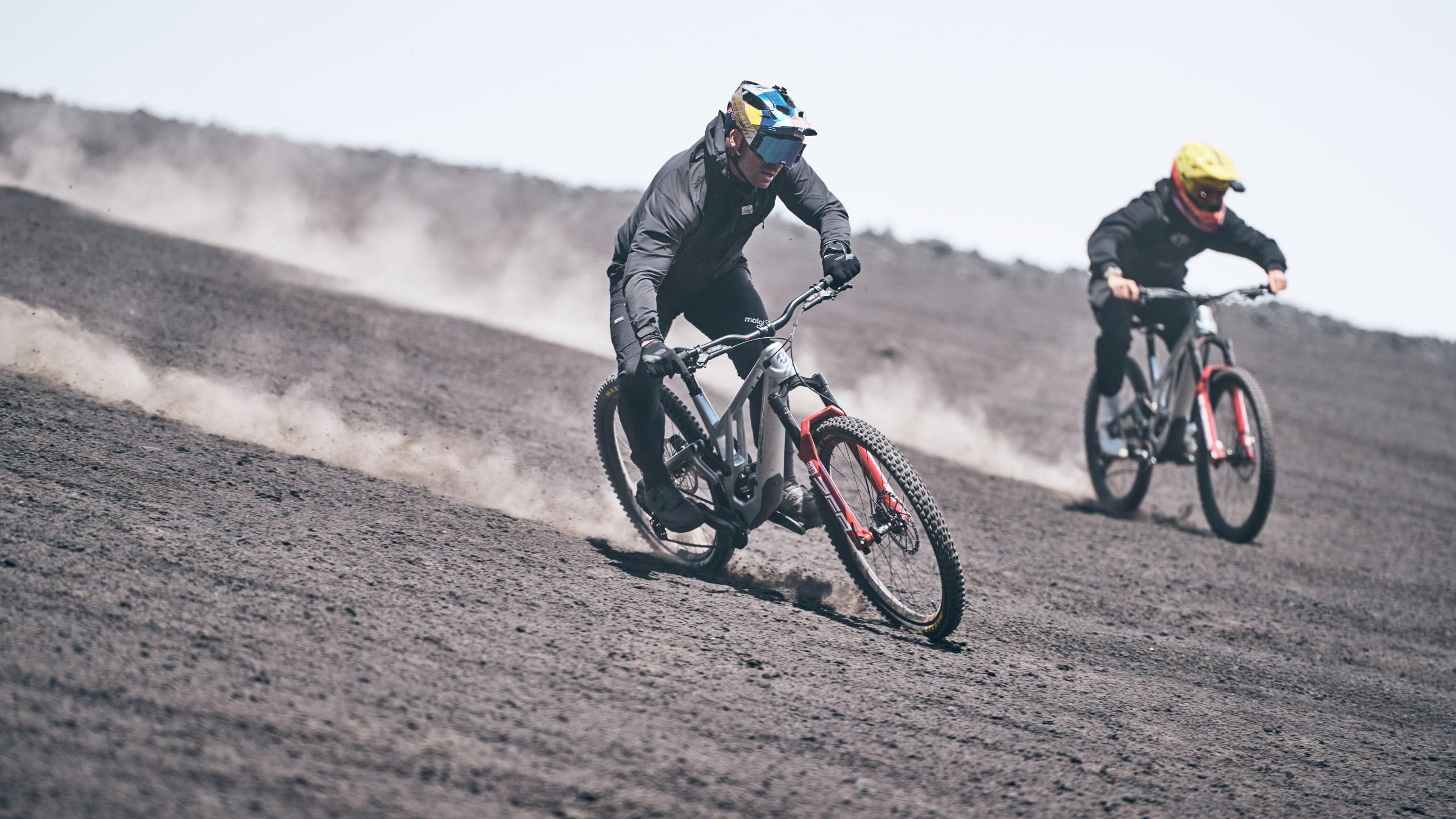 Mountain bike riders descending volcanic terrain, creating dust trails. Outdoor adventure, extreme sports, downhill biking, volcanic landscape. Mountain Bike United.