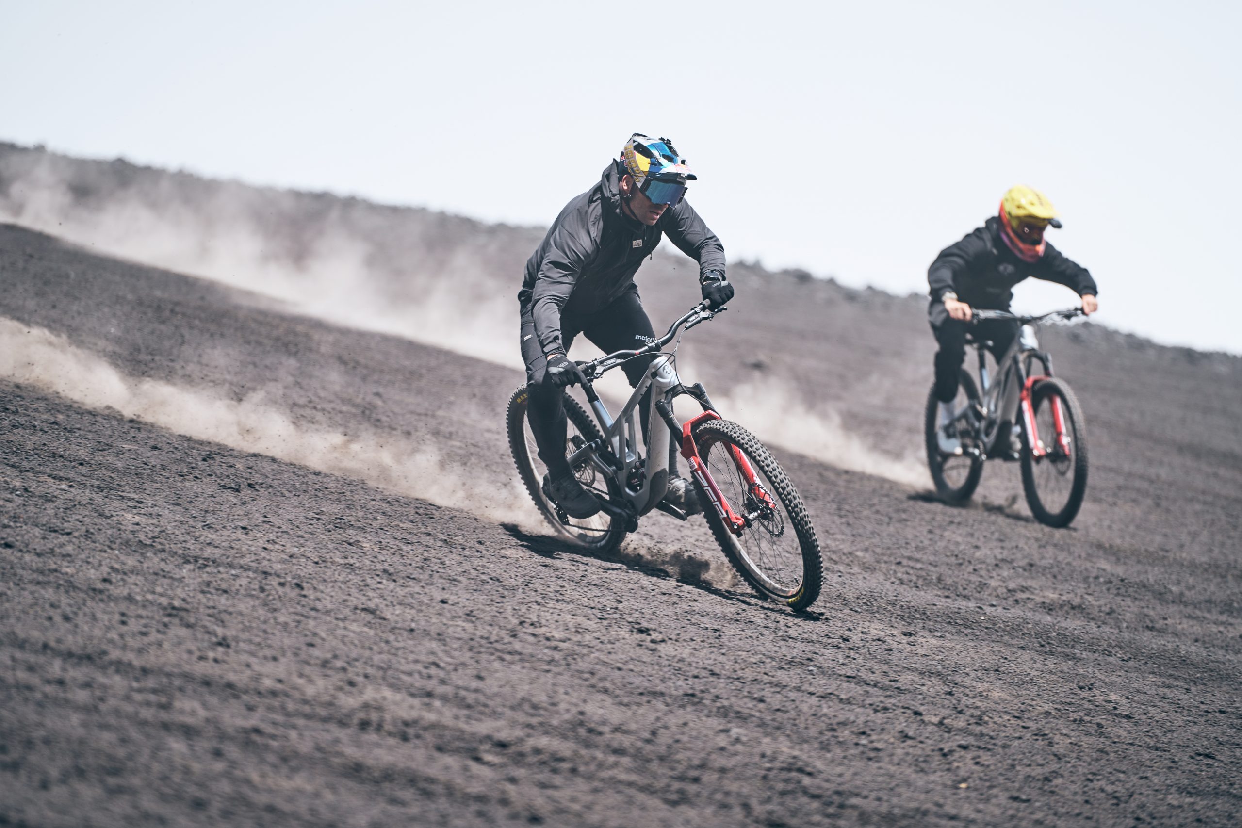 Mountain bike riders descending volcanic terrain, creating dust trails. Outdoor adventure, extreme sports, downhill biking, volcanic landscape. Mountain Bike United.