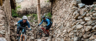 Two cyclists navigate a rocky village trail, showcasing mountain biking app features for tracking and exploring challenging routes. Mountain Bike United.