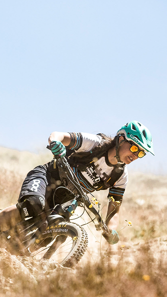 Female mountain biker navigating a trail using a mountain biking app for guidance and tracking in a sunny, rugged landscape. Mountain Bike United.
