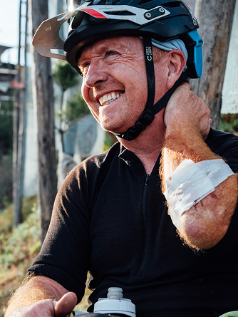 Man in helmet resting after mountain biking, smiling with makeshift bandage on arm. Mountain biking app. Mountain Bike United.