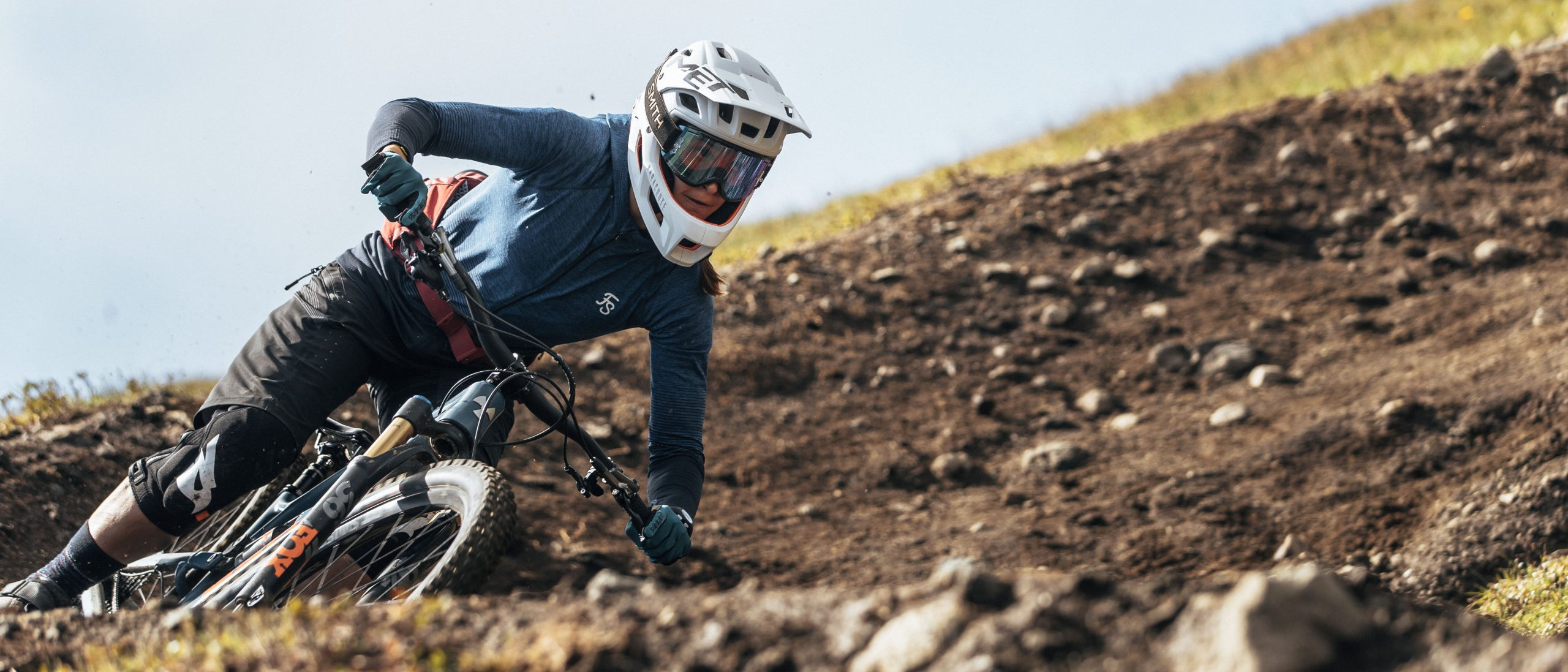 Mountain biker taking a sharp turn on a dirt trail downhill, wearing a helmet and protective gear, showcasing extreme sports adventure. Mountain Bike United app. Find mountain bike trails. Plan and share rides. Discover and join events and races. Record your rides directly in app. Strava mountain bike.