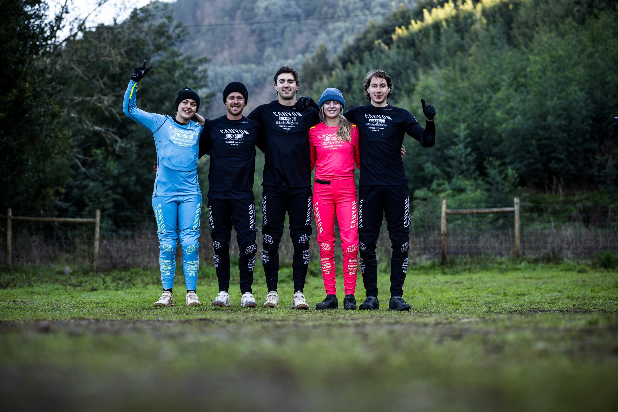 Canyon CLLCTV Gravity Team members posing outdoors in branded attire, showcasing teamwork and unity in a forested setting. Mountain Bike United.