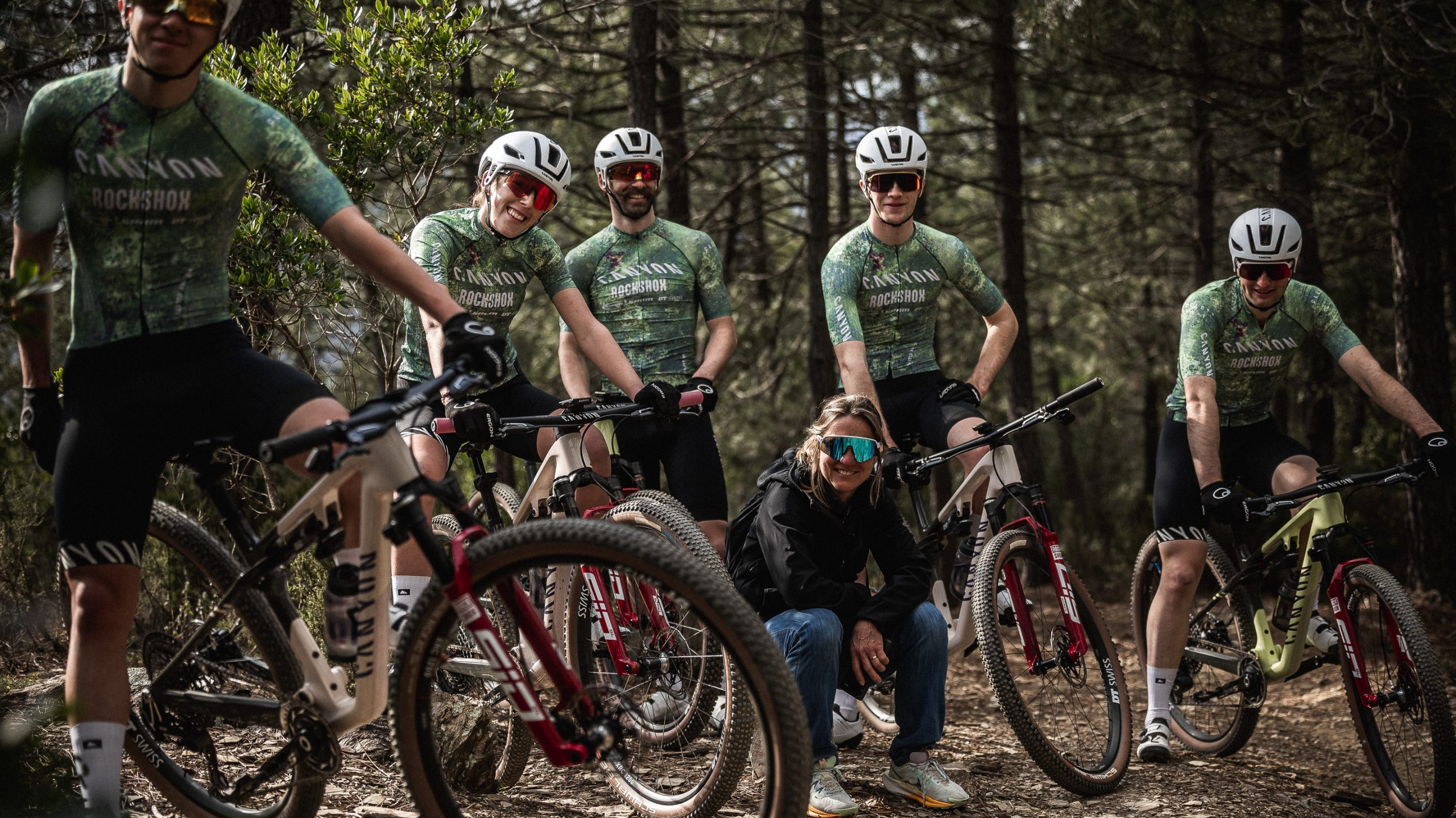 Cycling team posing with mountain bikes in forest trail, wearing helmets and jerseys. Outdoor adventure, sports gear, mountain biking enthusiasts. Mountain Bike United.