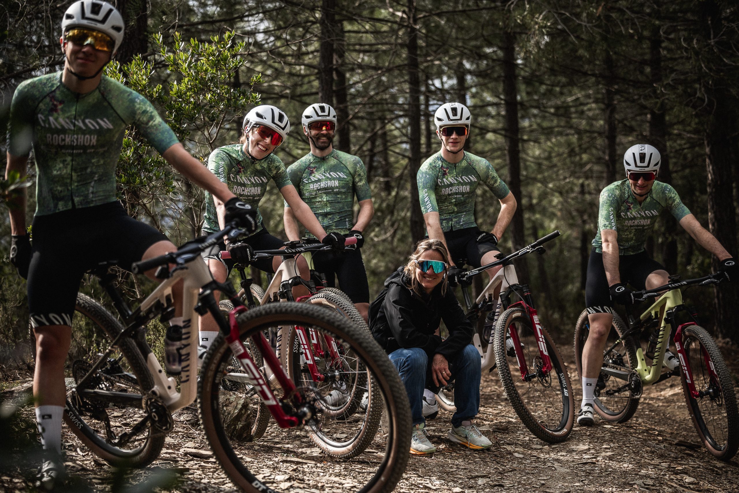 Cycling team posing with mountain bikes in forest trail, wearing helmets and jerseys. Outdoor adventure, sports gear, mountain biking enthusiasts. Mountain Bike United.