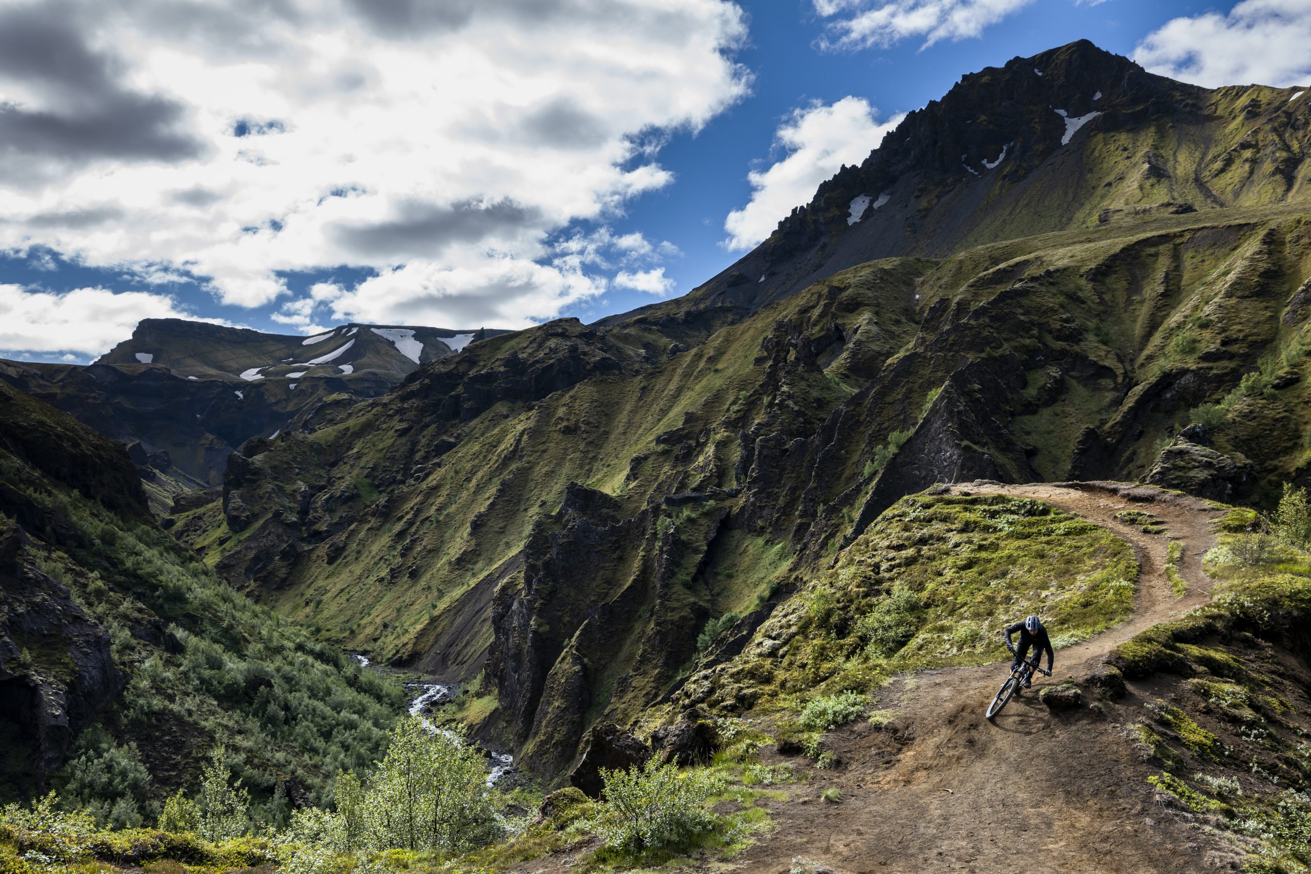 Mountain biker on a trail beside lush cliffs, reminiscent of Andrew Neethling's Journey to the Centre of the Earth adventure. Mountain Bike United.