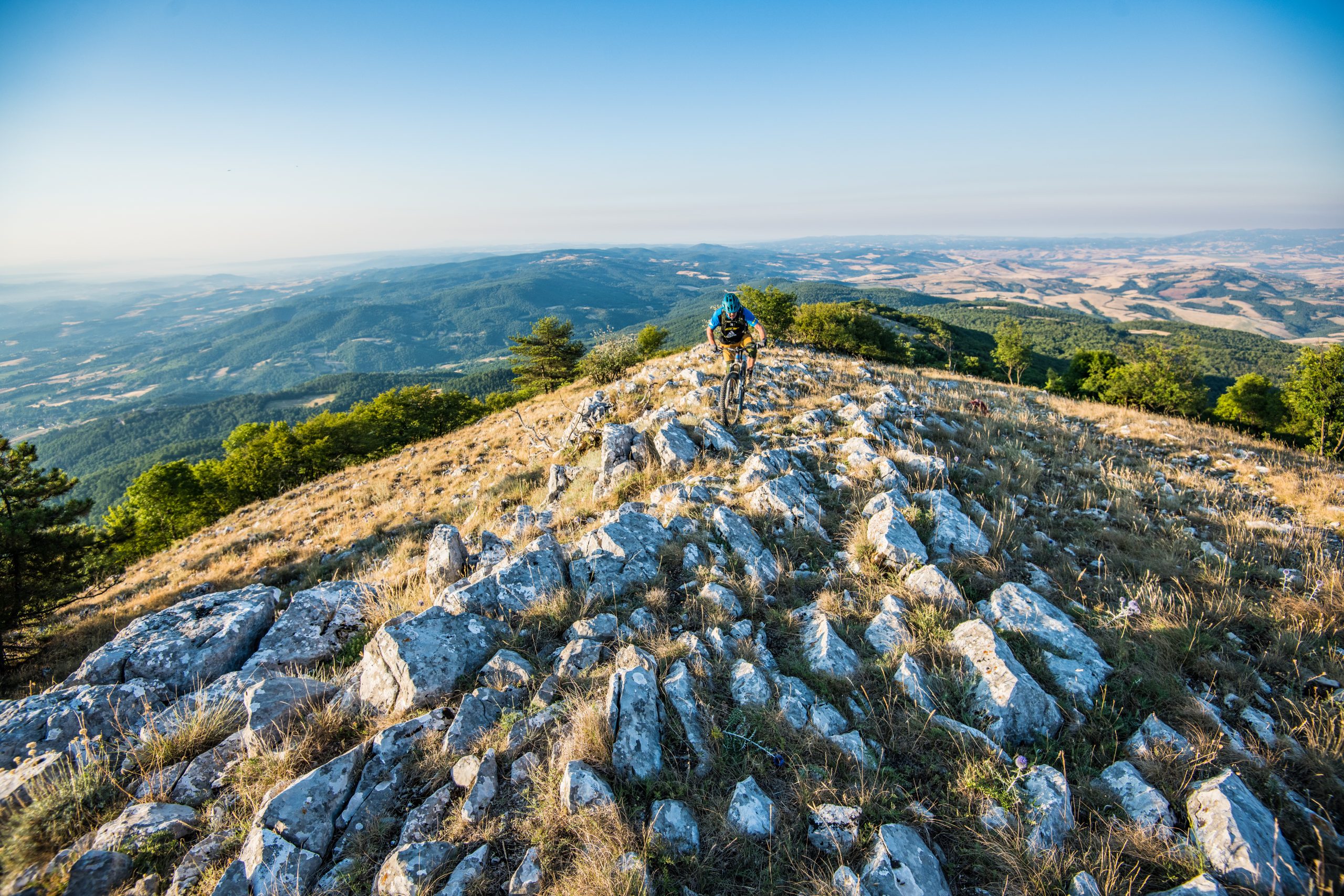Cyclist on rocky trail in Umbria, Italy, during Once Upon A Ride In Umbria event with Hans Rey, scenic landscape in the background. Mountain Bike United.