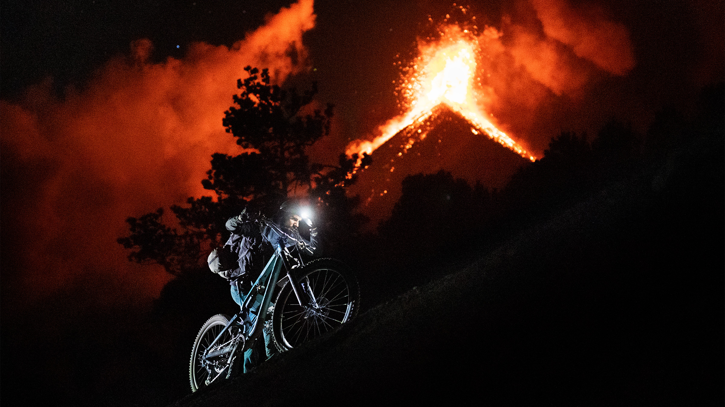 Kilian Bron cycling near Fuego volcano eruption, showcasing adventure sports and extreme biking against a fiery backdrop. Mountain Bike United.