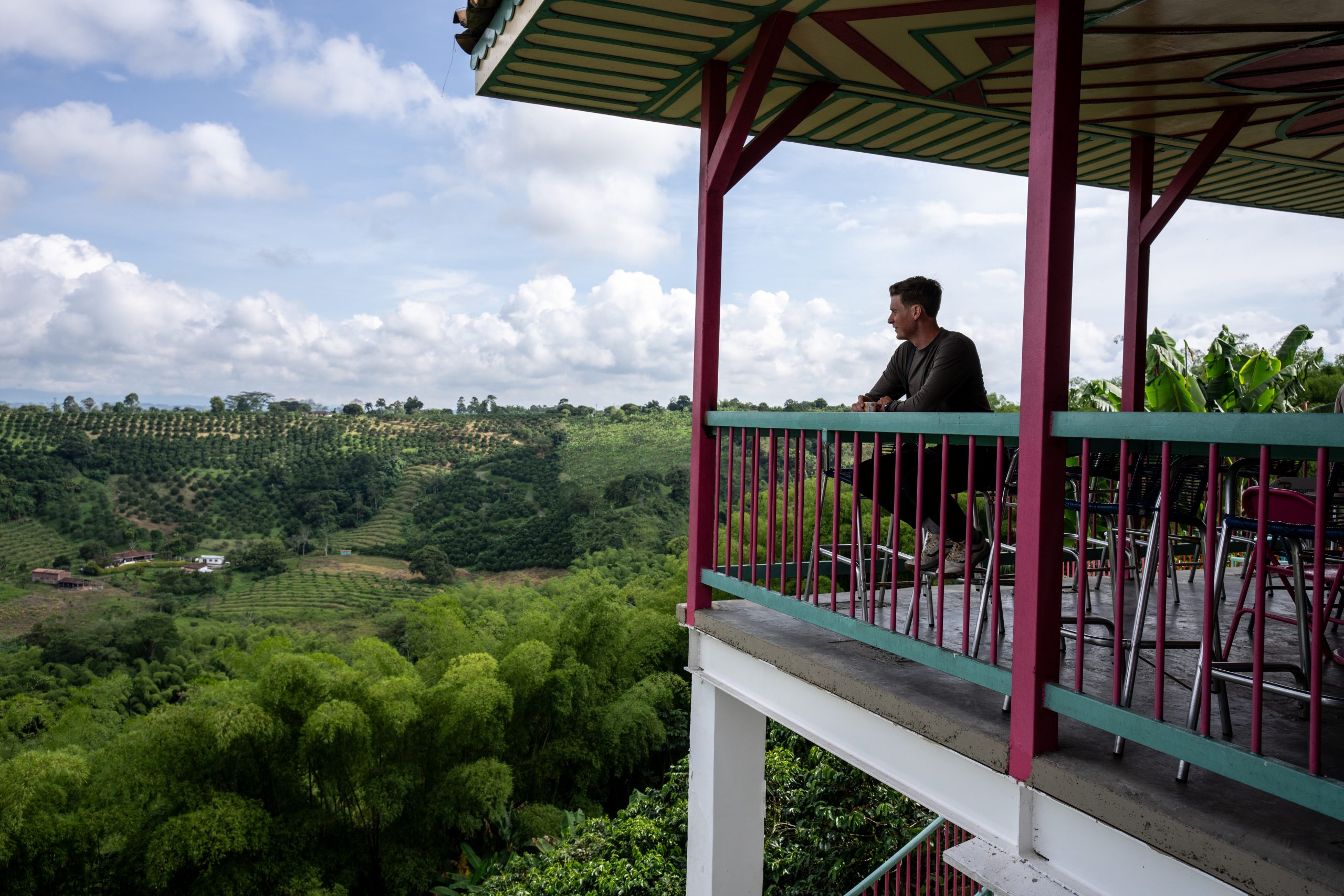 Man enjoying scenic Colombian landscape from a colorful balcony, highlighting the Taste of Colombia with Scotty Laughland experience. Mountain Bike United.