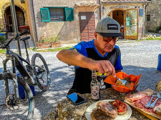 Man enjoying local cuisine in an Umbrian village with a mountain bike nearby, relating to Once Upon A Ride In Umbria with Hans Rey. Mountain Bike United.
