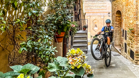 Cyclist performs a wheelie in an Umbrian alley, showcasing the adventure theme of Once Upon A Ride In Umbria with Hans Rey. Mountain Bike United.