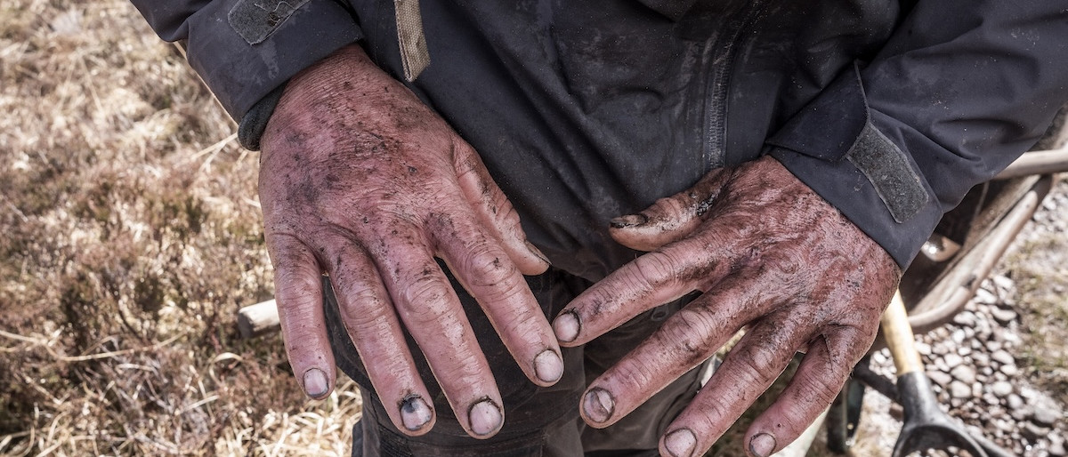 Trail builder's muddy hands highlight manual work essential for managing trails. Mountain Bike United.