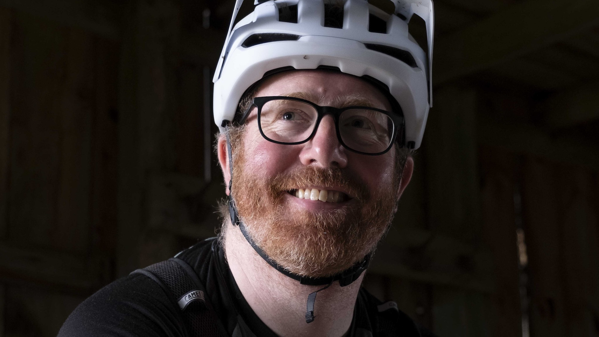 Man wearing a white bicycle helmet and glasses, smiling indoors, ideal for cycling safety and gear promotion. Mountain Bike United. MTB event management solutions.