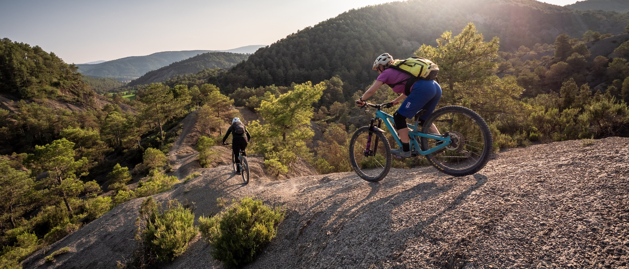 Mountain bikers navigate rugged trails on a scenic hillside, showcasing effective management of mountain bike trails. Mountain Bike United app. Manage mountain bike trails. Fund mountain bike trails. Manage trail volunteers. Control route updates. Mountain bike dig days.