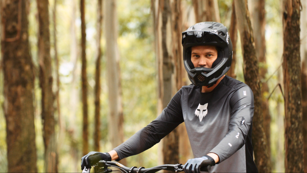 Mountain biker in helmet riding through a forest, showcasing skills in Greg Minnaar Swapping Lines technique. Mountain Bike United.
