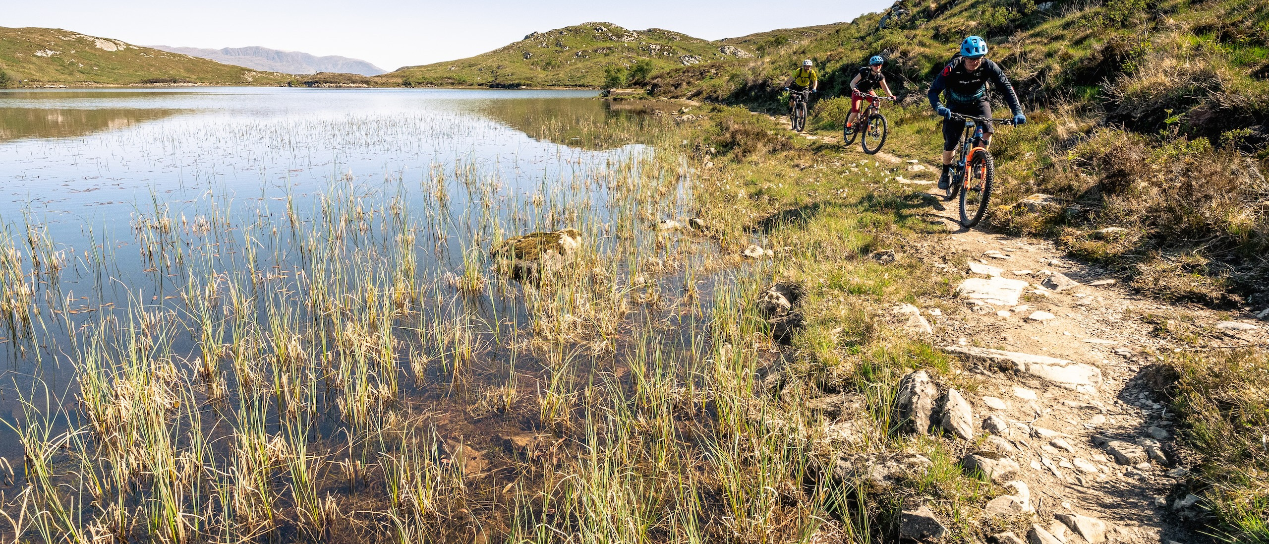 Mountain bikers riding next to a loch in Scotland