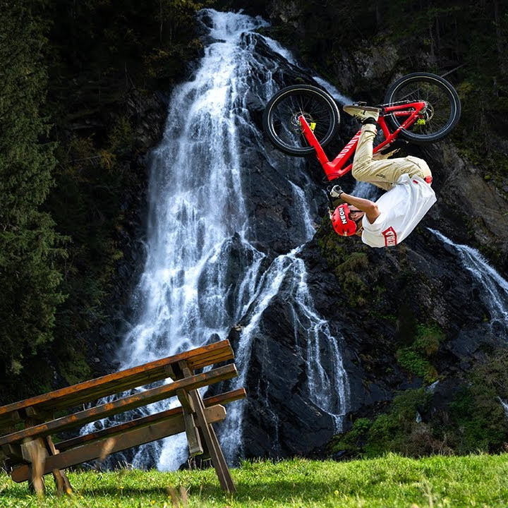 Extreme sports cyclist performing a backflip on a mountain bike in front of a waterfall, highlighting adventure and skills. Keywords: Gabriel Wibmer, mountain biking. Mountain Bike United.