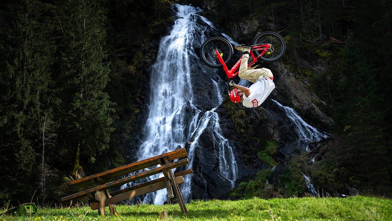 Extreme sports cyclist performing a backflip on a mountain bike in front of a waterfall, highlighting adventure and skills. Keywords: Gabriel Wibmer, mountain biking. Mountain Bike United.
