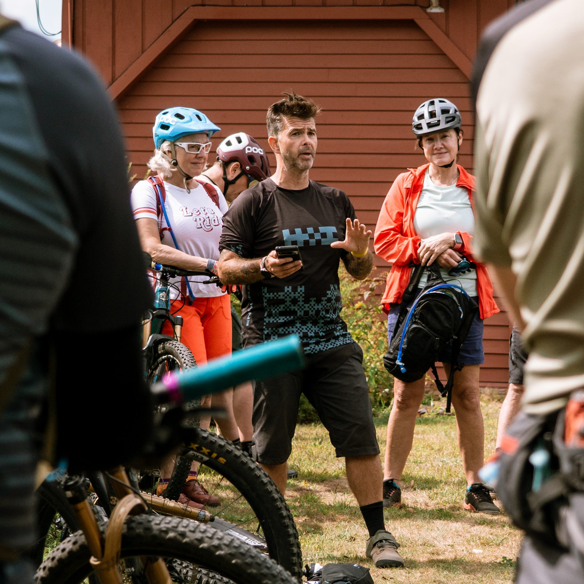 Group discussion on organizing an MTB event. Cyclists gather outdoors with bikes in the foreground, focusing on planning and logistics. Mountain Bike United.