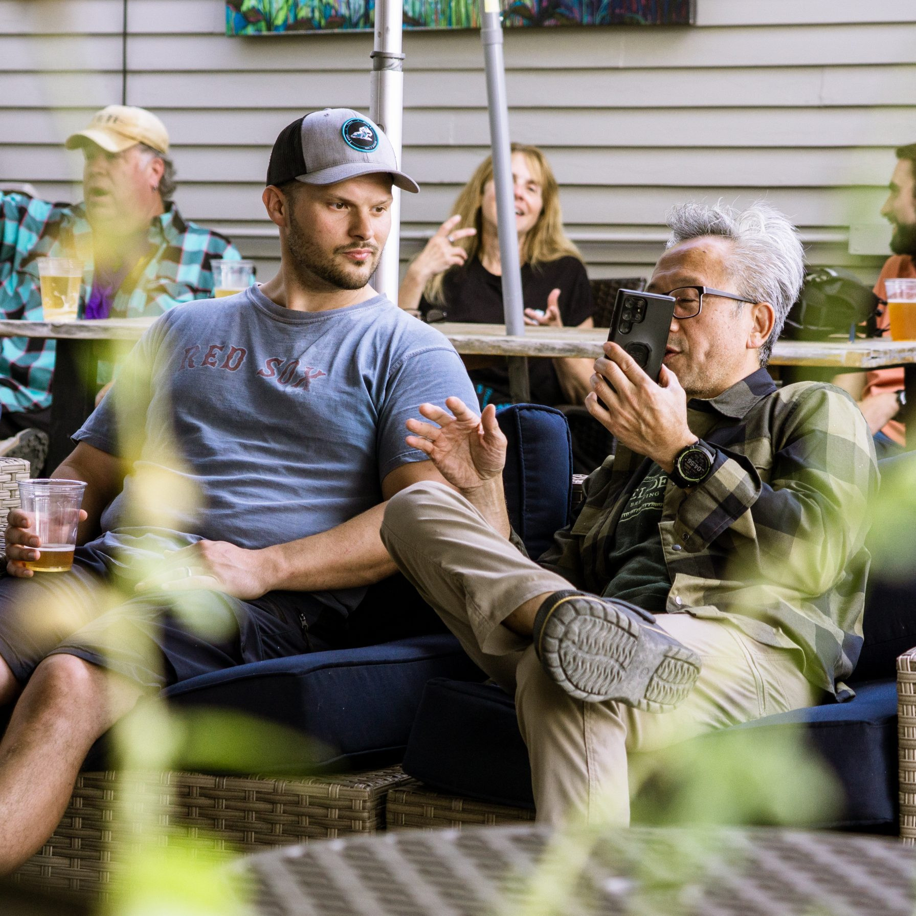 Men discussing at an outdoor event planning meeting, potential MTB event organization, casual setting with drinks, strategic conversation. Mountain Bike United.