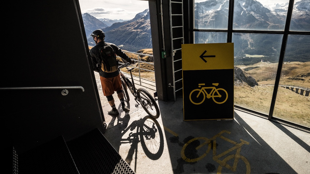 Cyclist exits building with bike, showcasing destination management tools for outdoor adventures. Mountain Bike United.