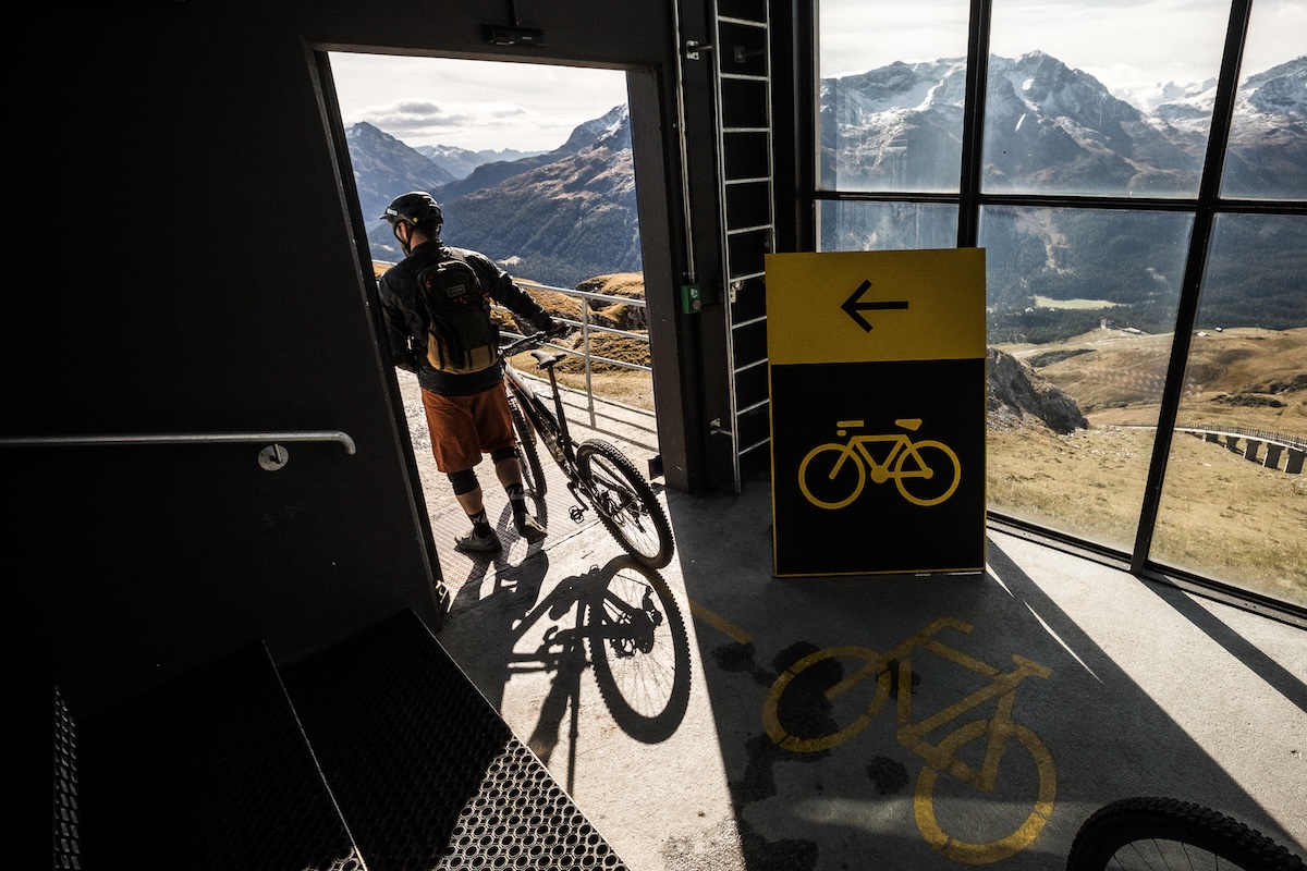 Cyclist exits building with bike, showcasing destination management tools for outdoor adventures. Mountain Bike United.