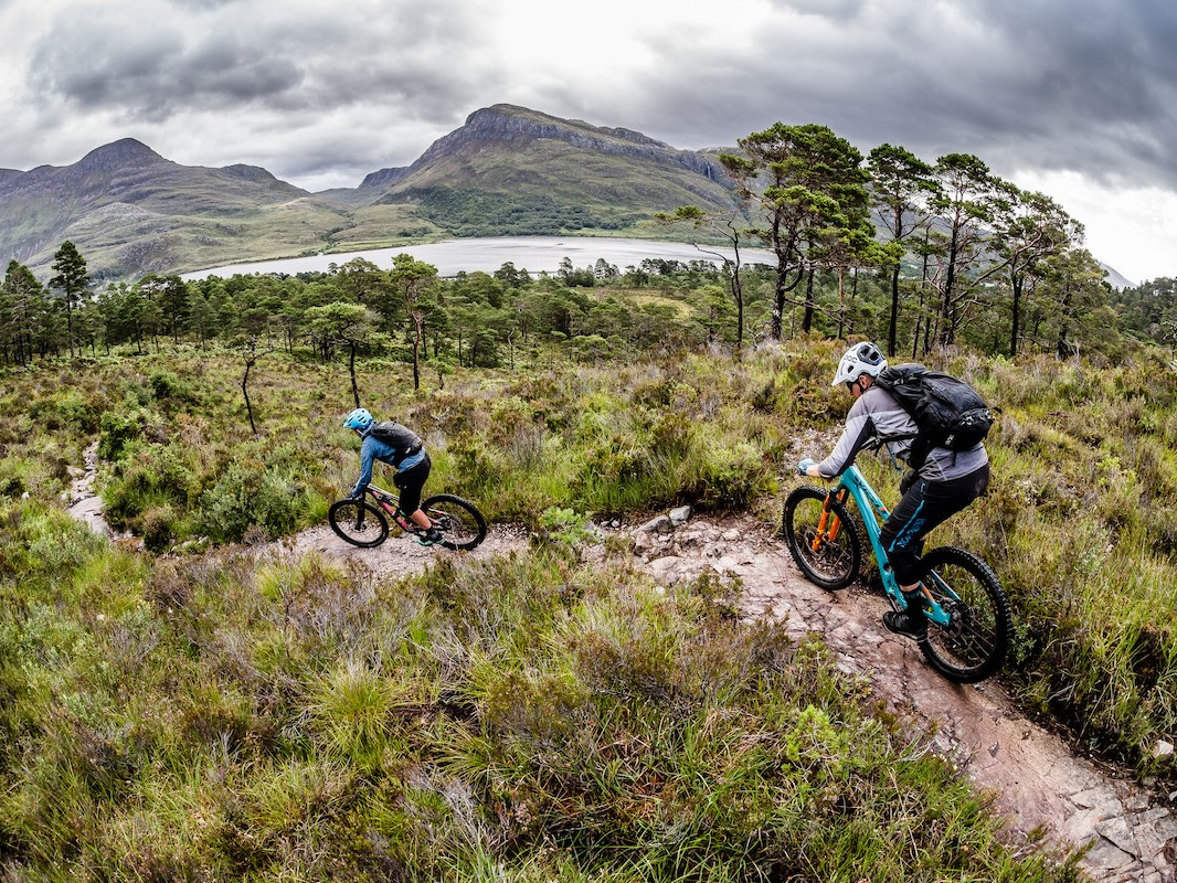 Mountain bikers on rugged trail with scenic backdrop, using self-guided tour tools. Mountain Bike United.