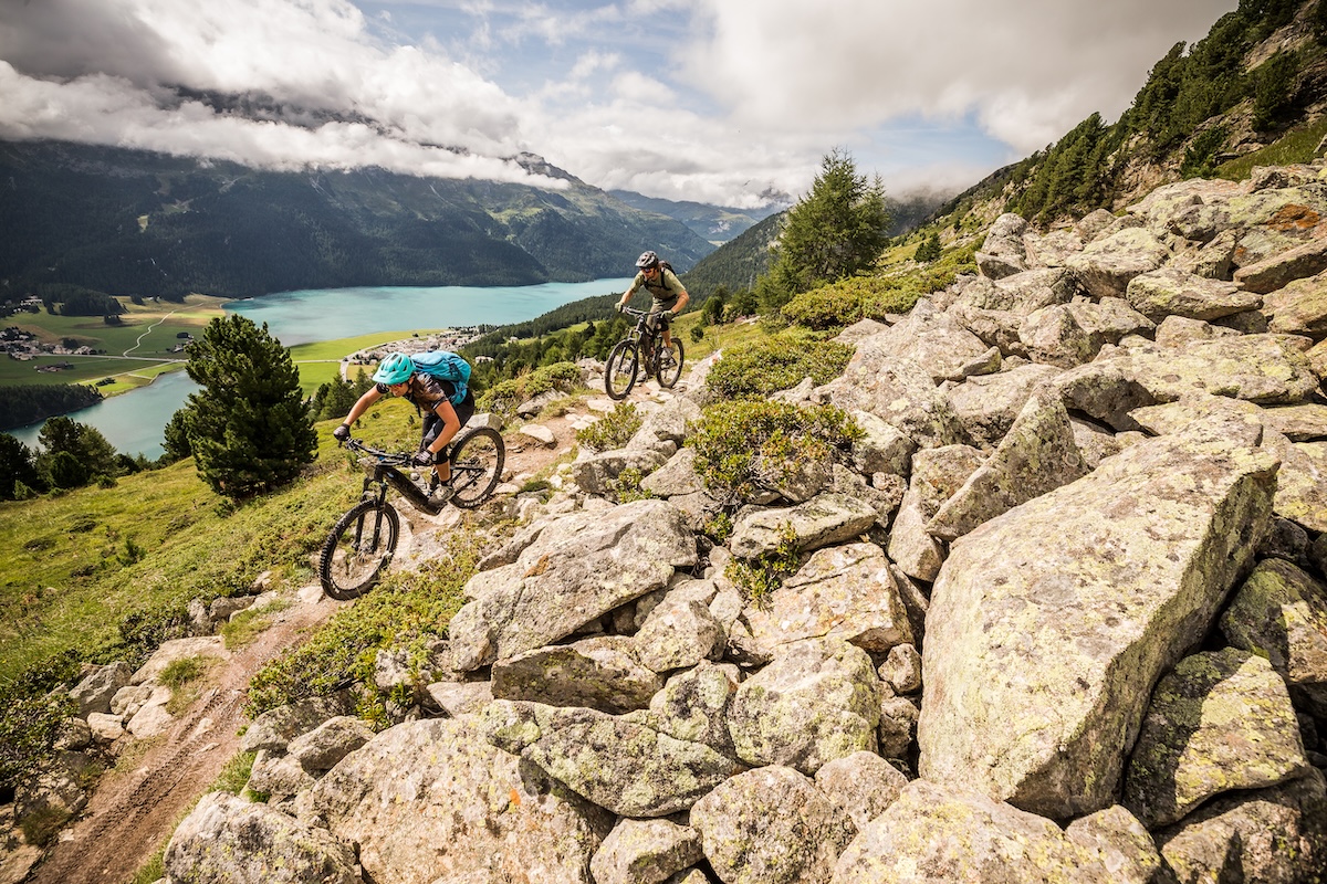 Mountain bikers navigating rocky trail by lake. Mountain Bike United.